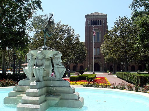 photo of large water fountain with statue on USC campus in front of a tall brick building and trees