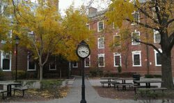 Photo of brick building on Rutgers New Brunswick campus with autumn trees and a standalone large clock on a pole in the foreground