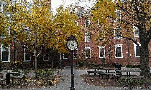 Photo of brick building on Rutgers New Brunswick campus with autumn trees and a standalone large clock on a pole in the foreground