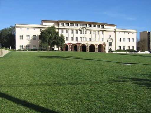 photo of an off-white brick campus building with a large, green lawn in front