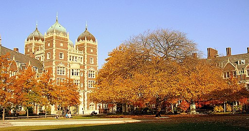 photo of tall brick university building with autumn leaves on trees in foreground