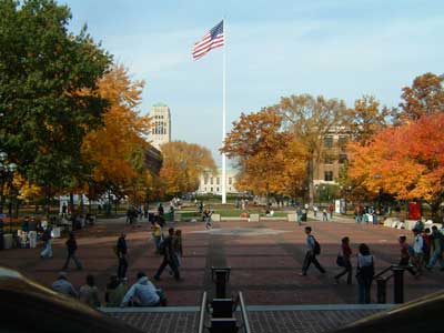 photo of University of Michigan Ann Arbor campus with brick quad, and flag pole in center. campus buildings and autumn trees surround.