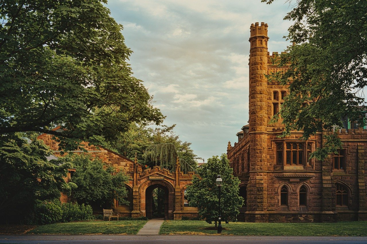 image of an idyllic campus setting with a brick church and a brick arcade, surrounding by green trees