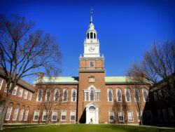 image shows a large brick university building with a clock tower in front of a blue sky