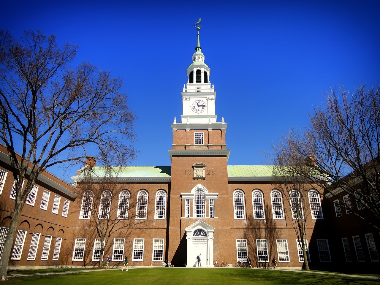 image shows a large brick university building with a clock tower in front of a blue sky