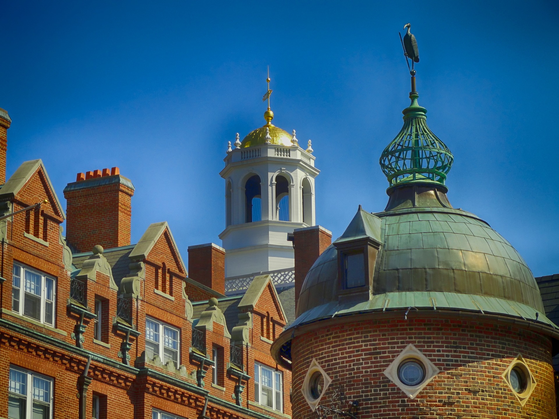 image of brick tower dome with spire in foreground and a gabled brick roof in background