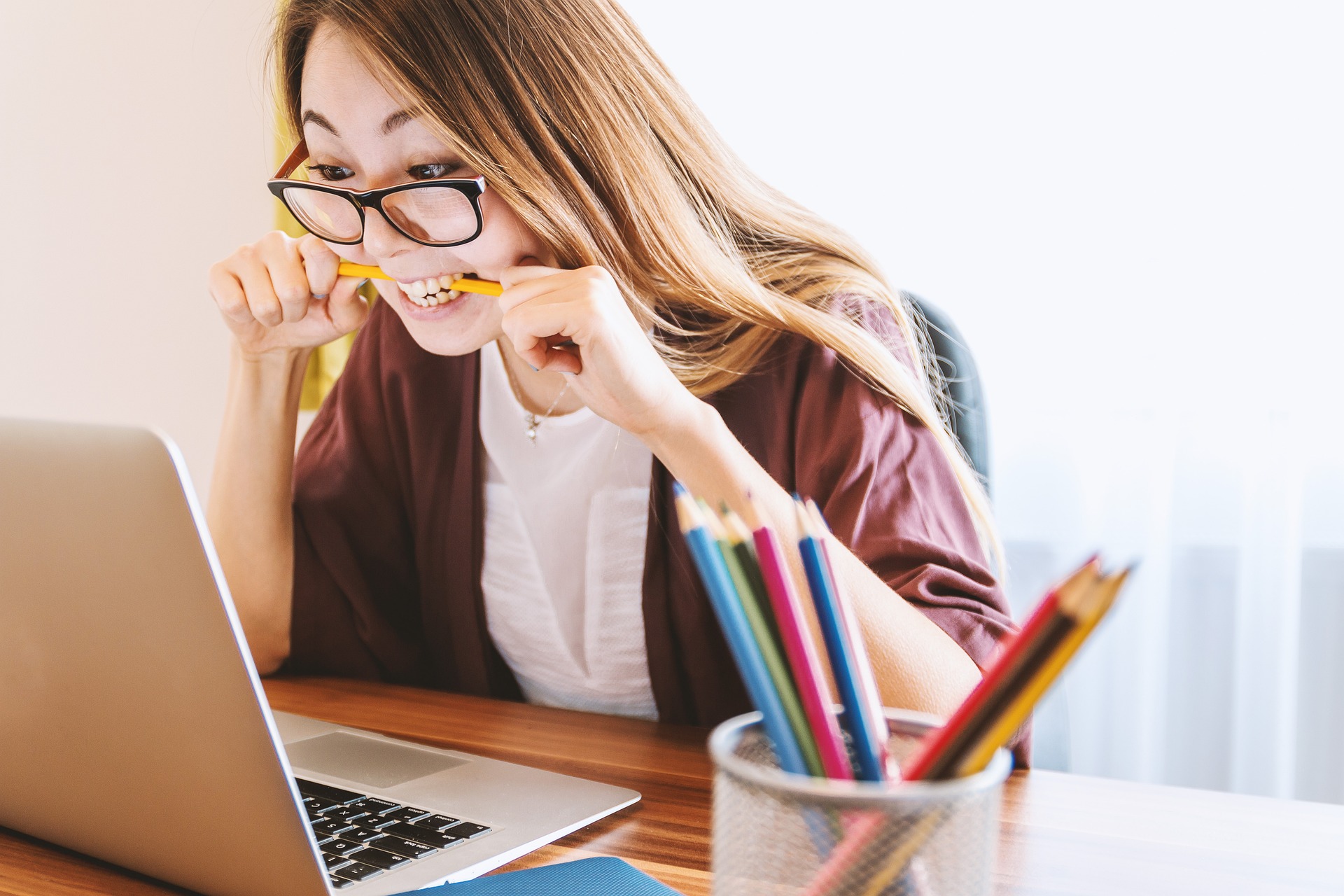 stressed young woman at laptop biting pencil