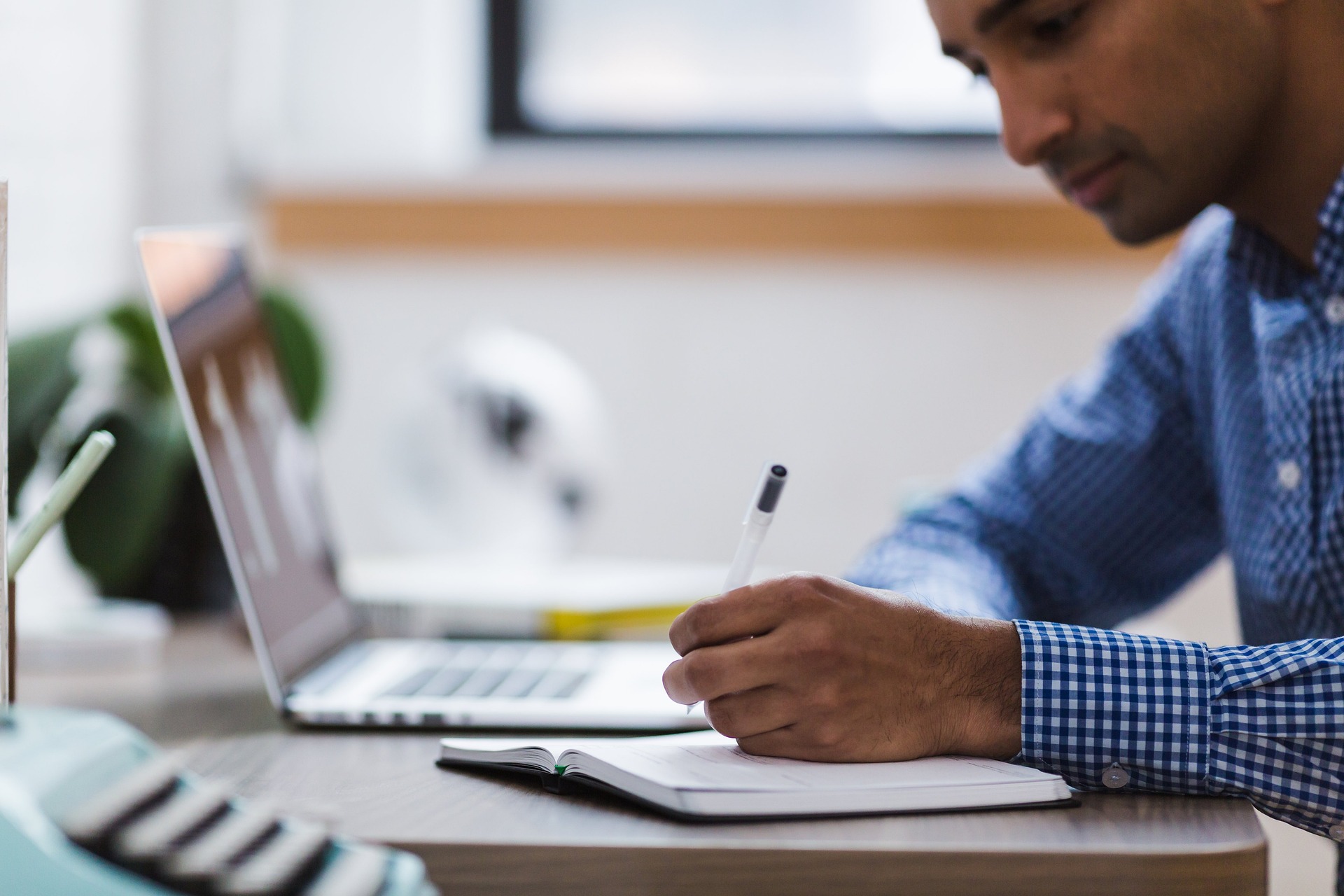 young man writing in a notebook in front of an open laptop