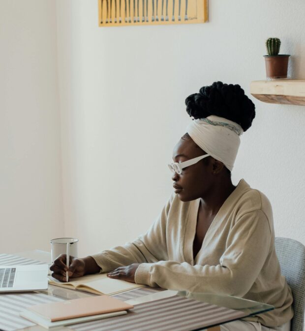 young woman writing at her desk in a notebook, next to an open laptop