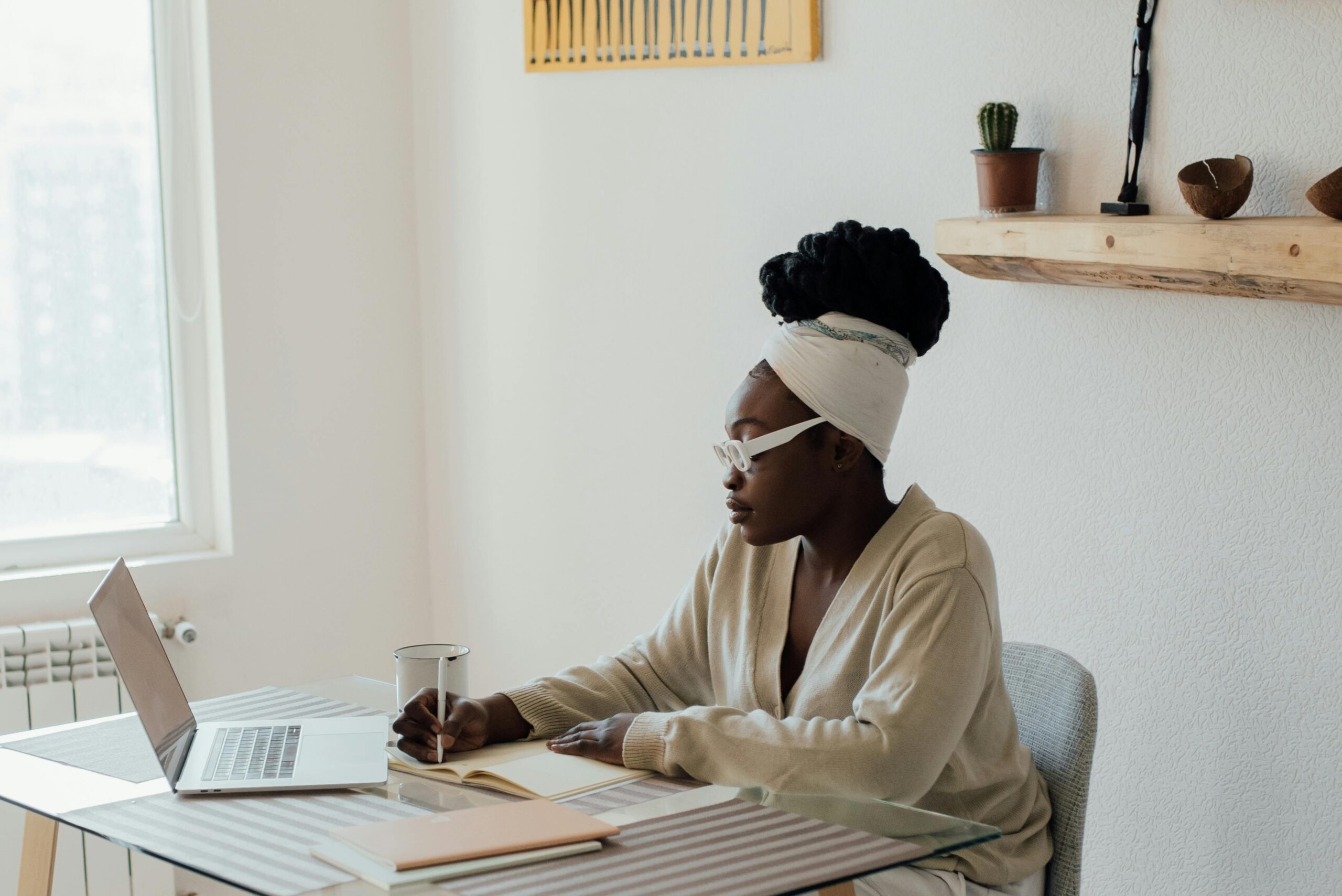 young woman writing at her desk in a notebook, next to an open laptop