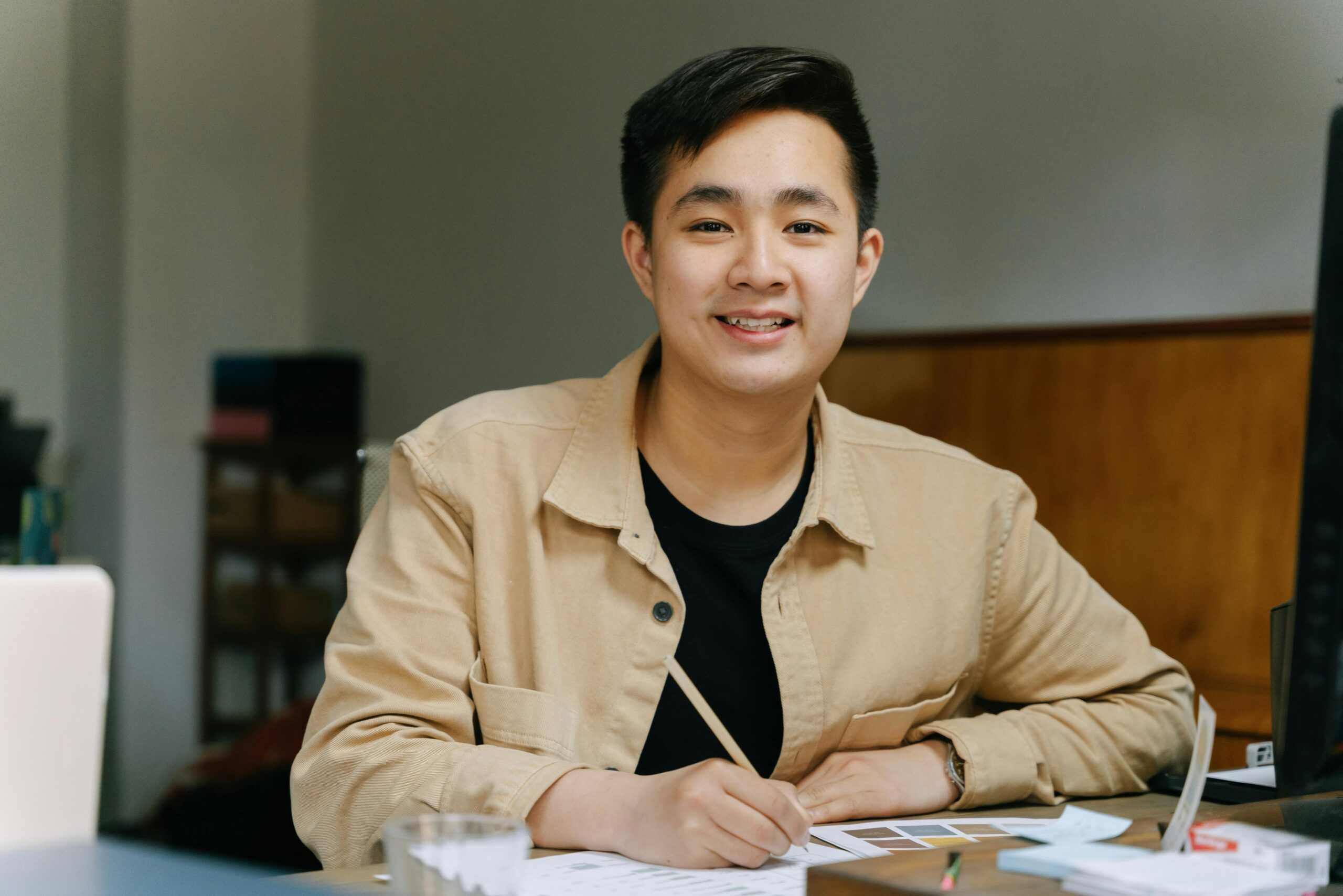 young man writing in notebook at a desk while smiling