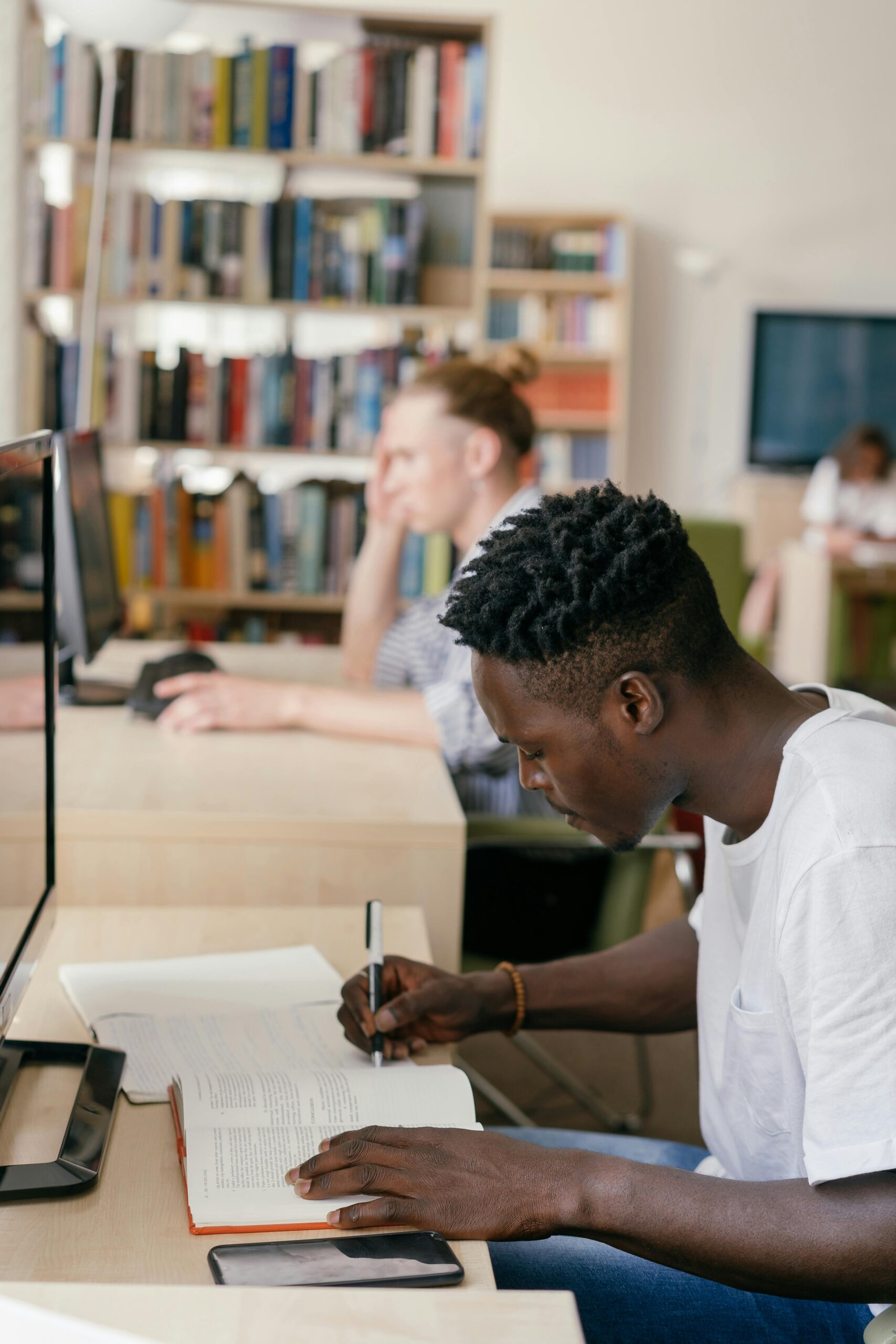 young man writing at a desk in front of a computer monitor