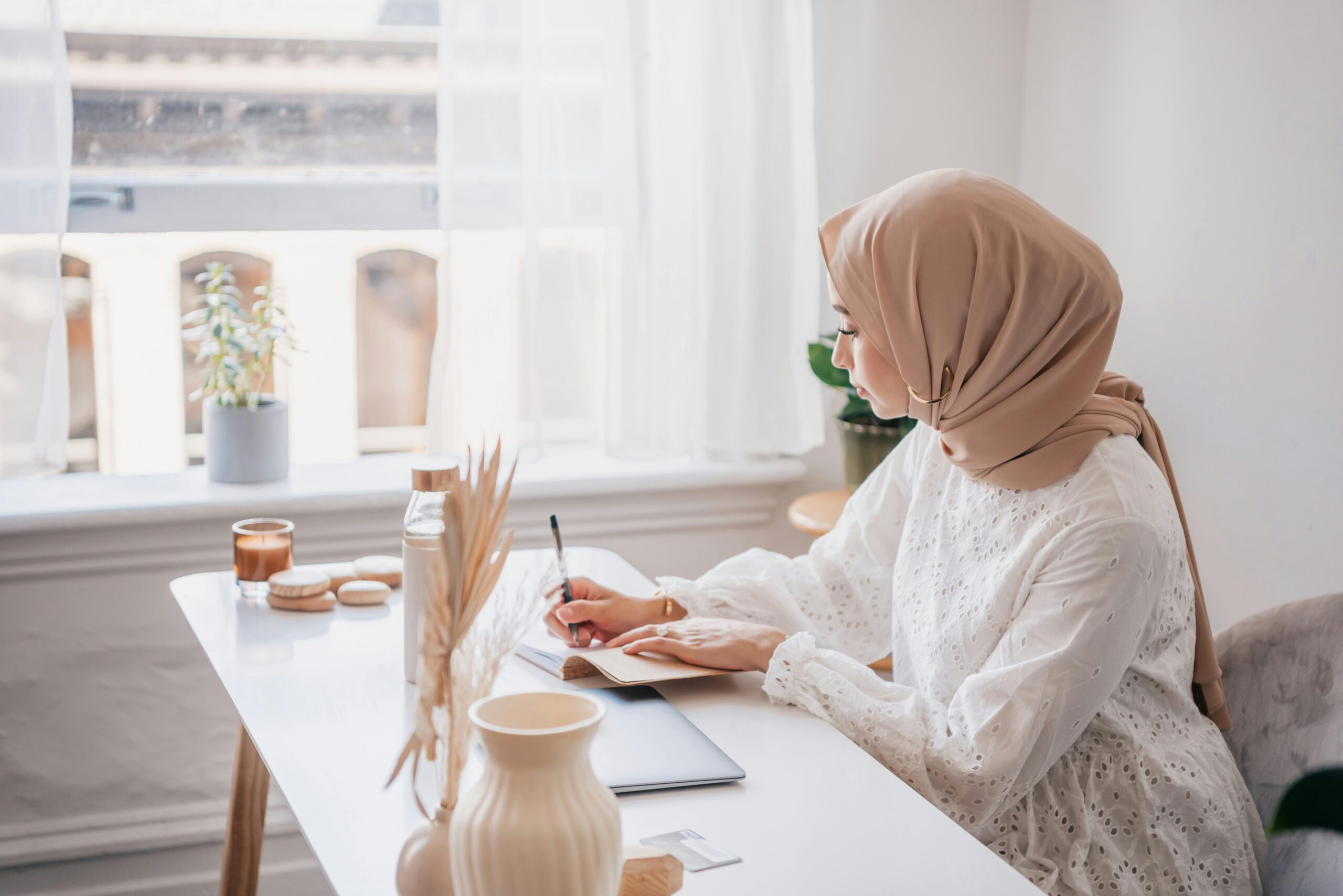 a young woman in a hijab writing in a notebook at a desk