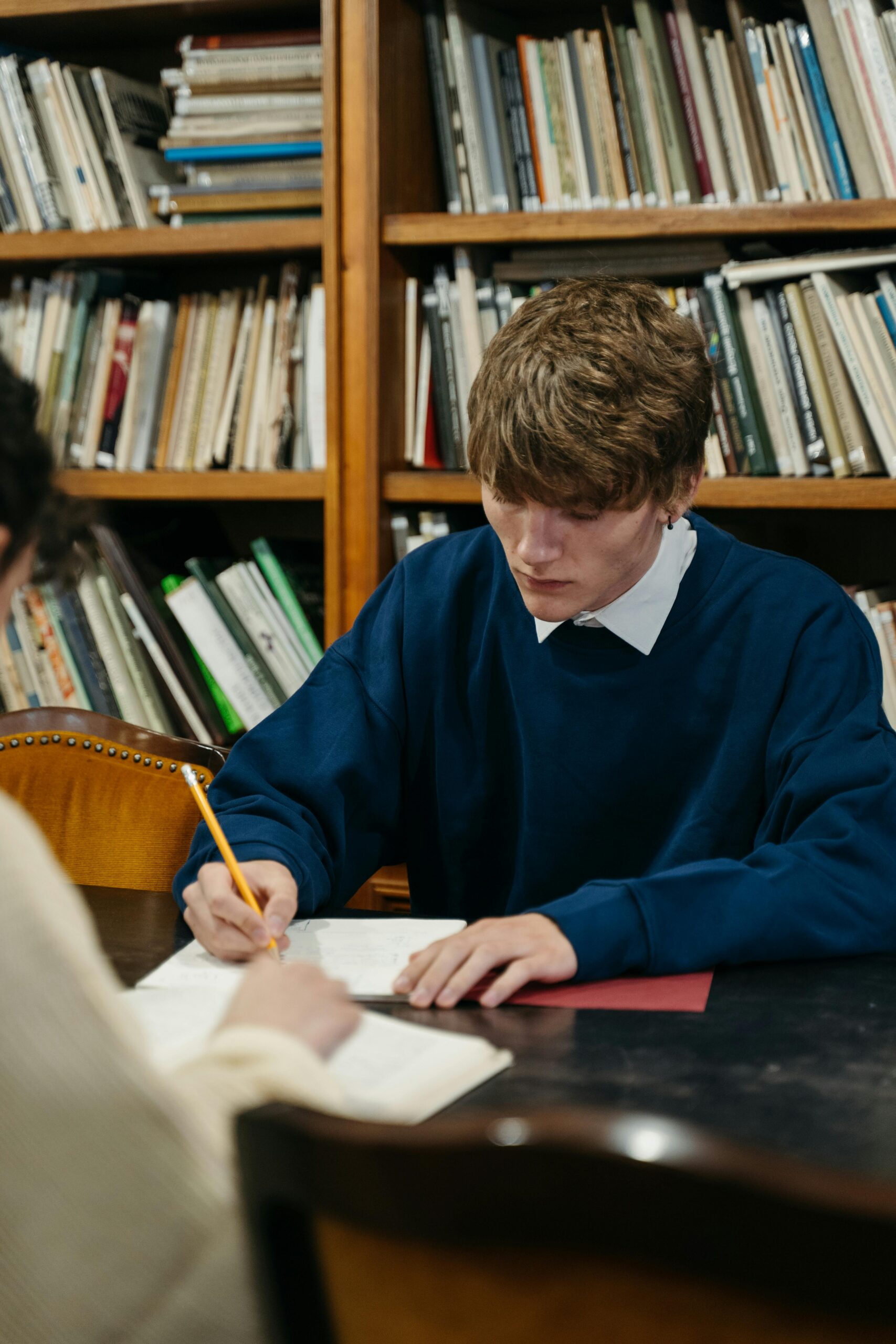 young man in a library writing in a notebook