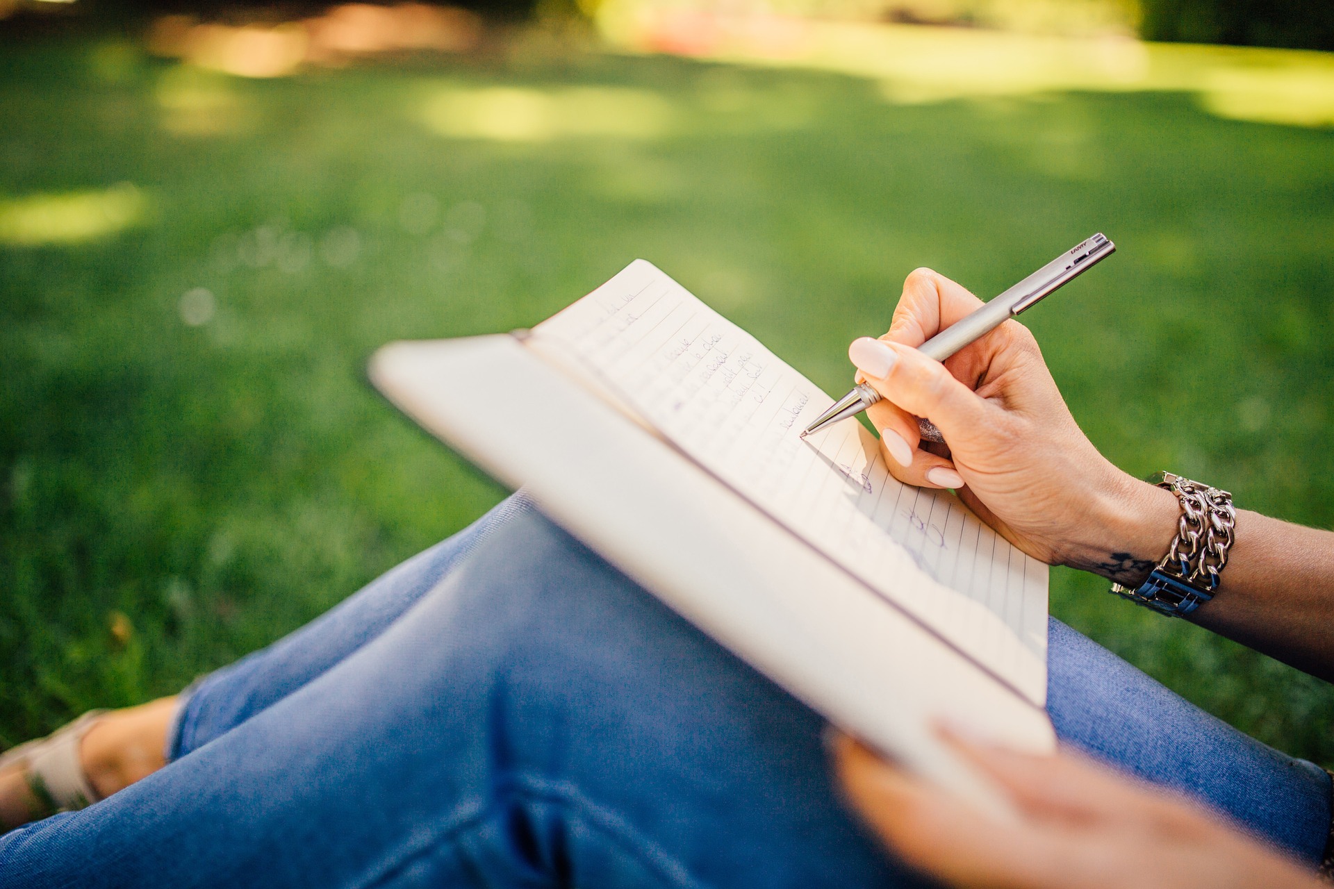 person sitting on grass writing, with only legs and hands in frame