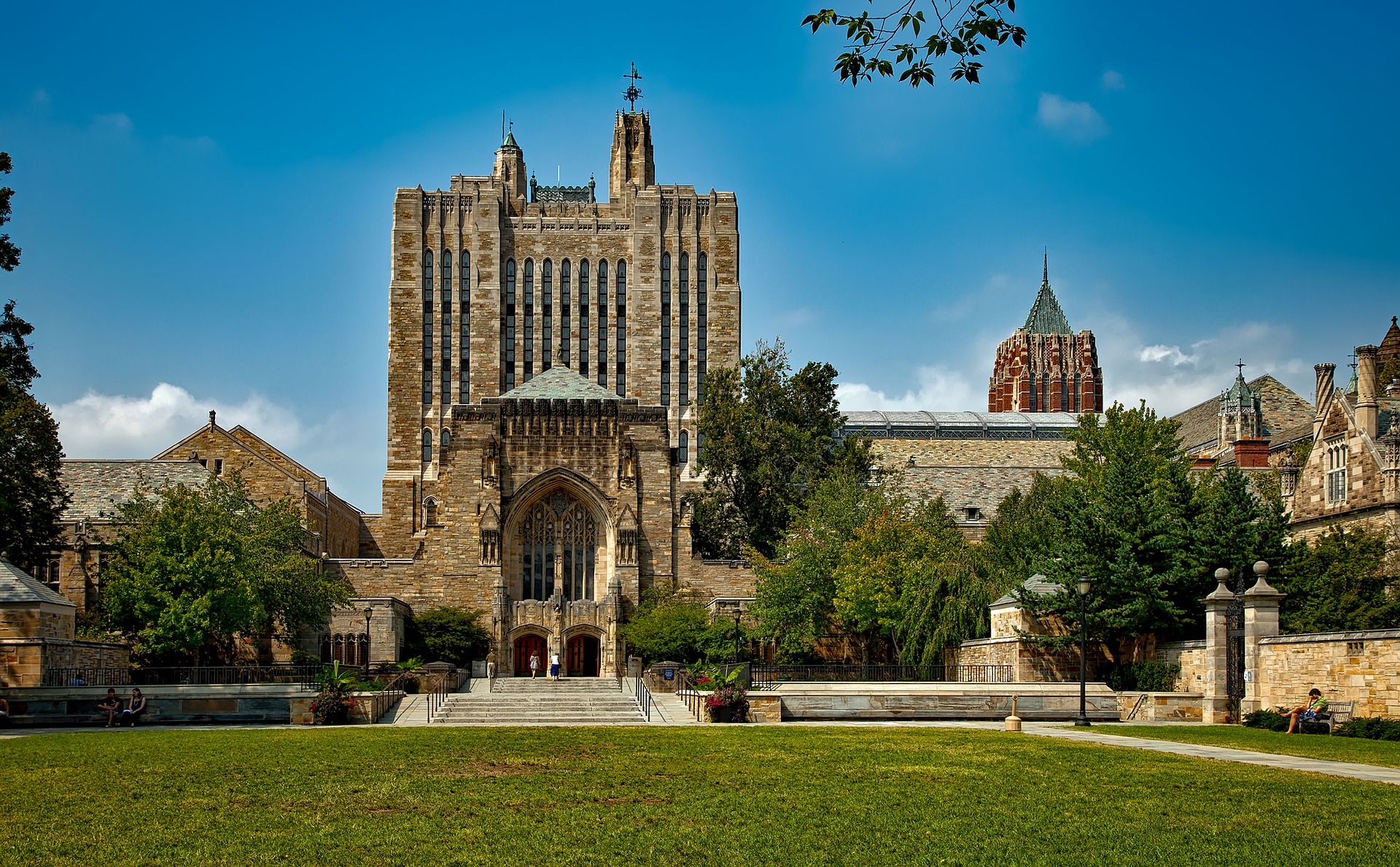 image of a grassy campus quad with a light-colored stone building in background with ornate, arched architecture