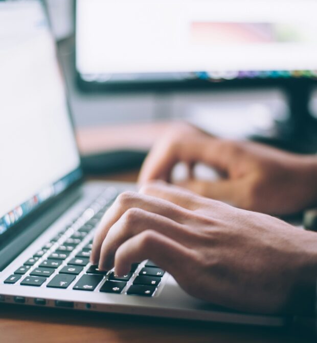 Close up of two hands typing on a laptop keyboard with blank document on screen.