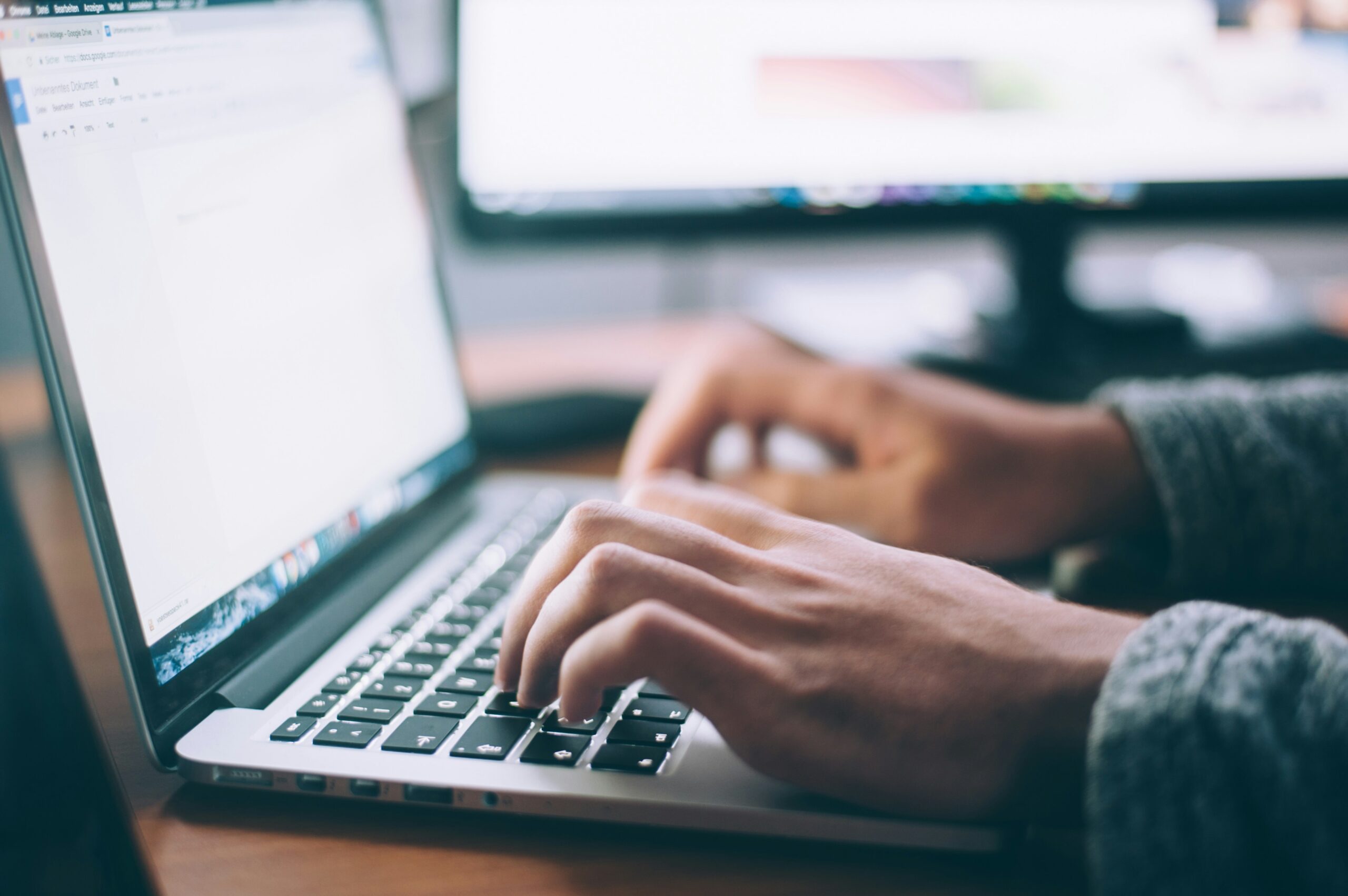 Close up of two hands typing on a laptop keyboard with blank document on screen.