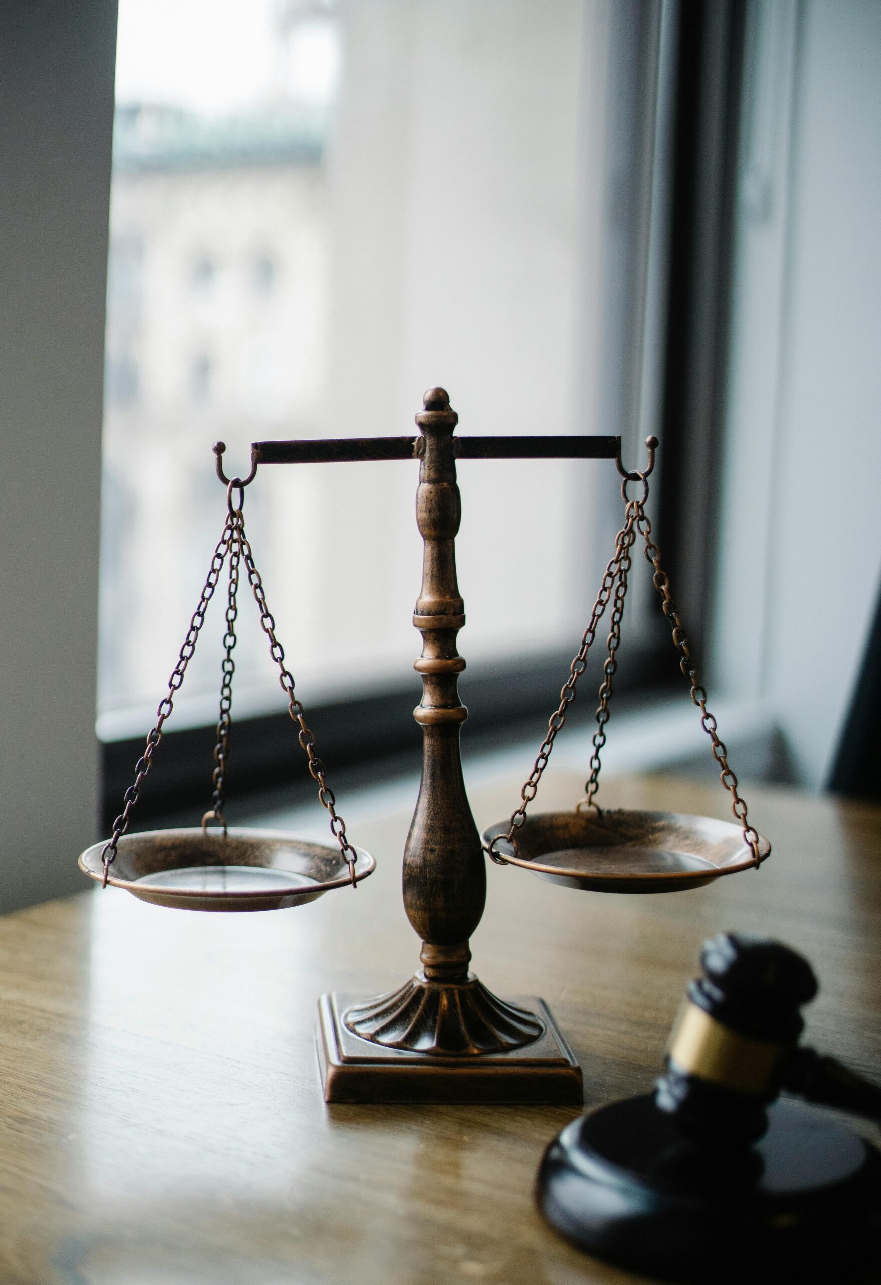 Brass balance scale on wooden desk next to window