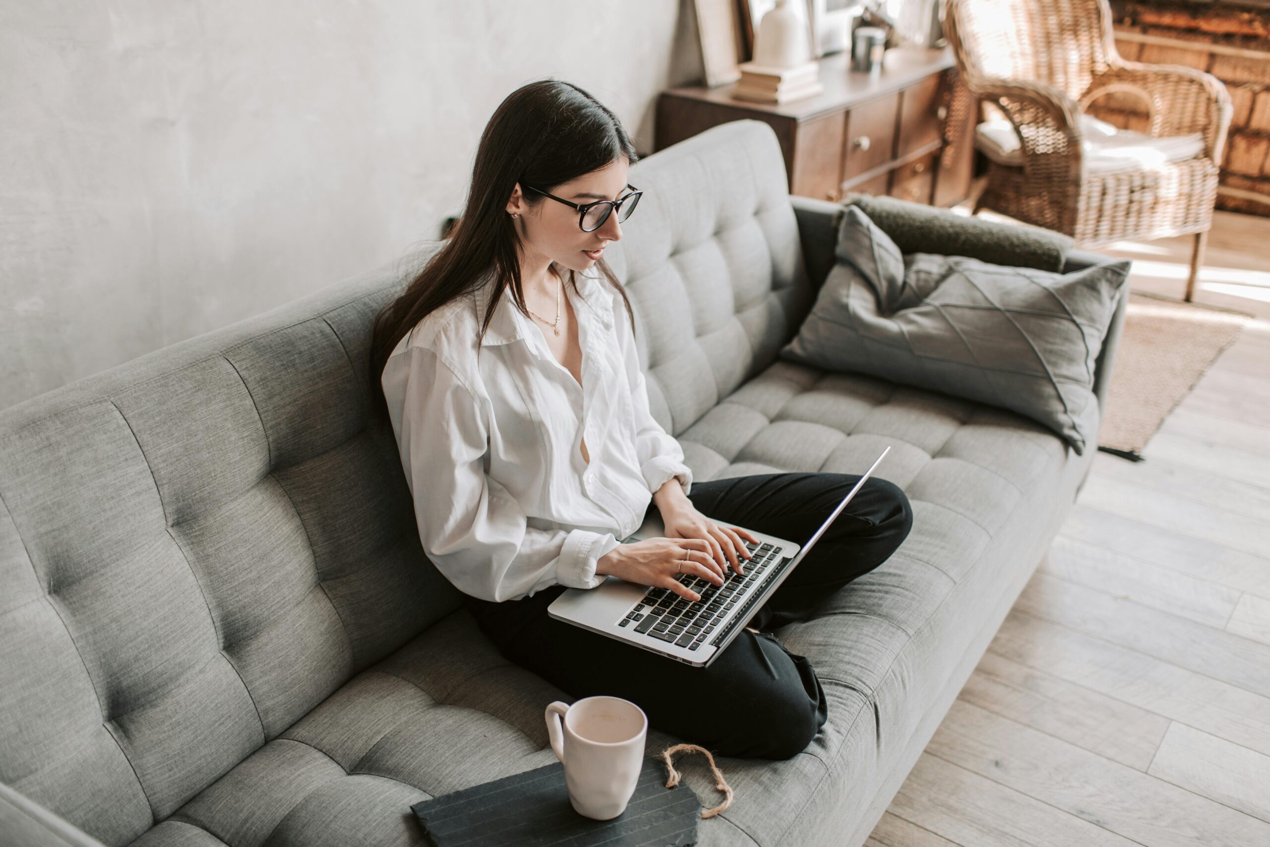 Woman in business attire sits on couch with laptop