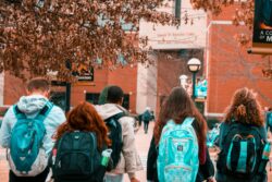 Five teenage students, wearing school bags on their shoulders, walk toward school.