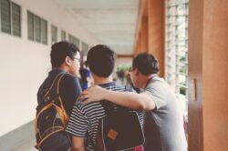 Two young boys stand in a college hallway, speaking with a staff member and asking a question.