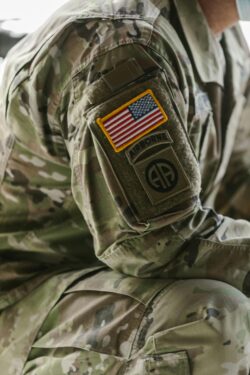 ALT text: Close-up of a military uniform sleeve with a U.S. flag patch and an "Airborne" insignia. The camouflage pattern suggests a disciplined and formal tone.