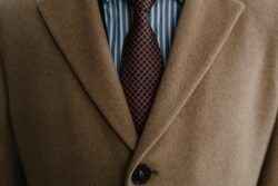 upclose of torso wearing a tan blazer with maroon red tie on top of a striped blue and white shirt
