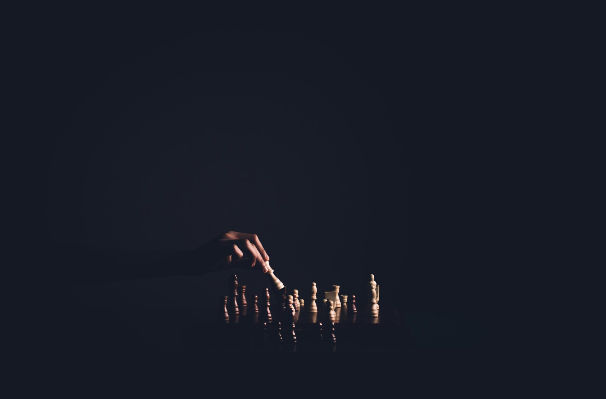 chess board dimly lit on a black background, hand moving the king