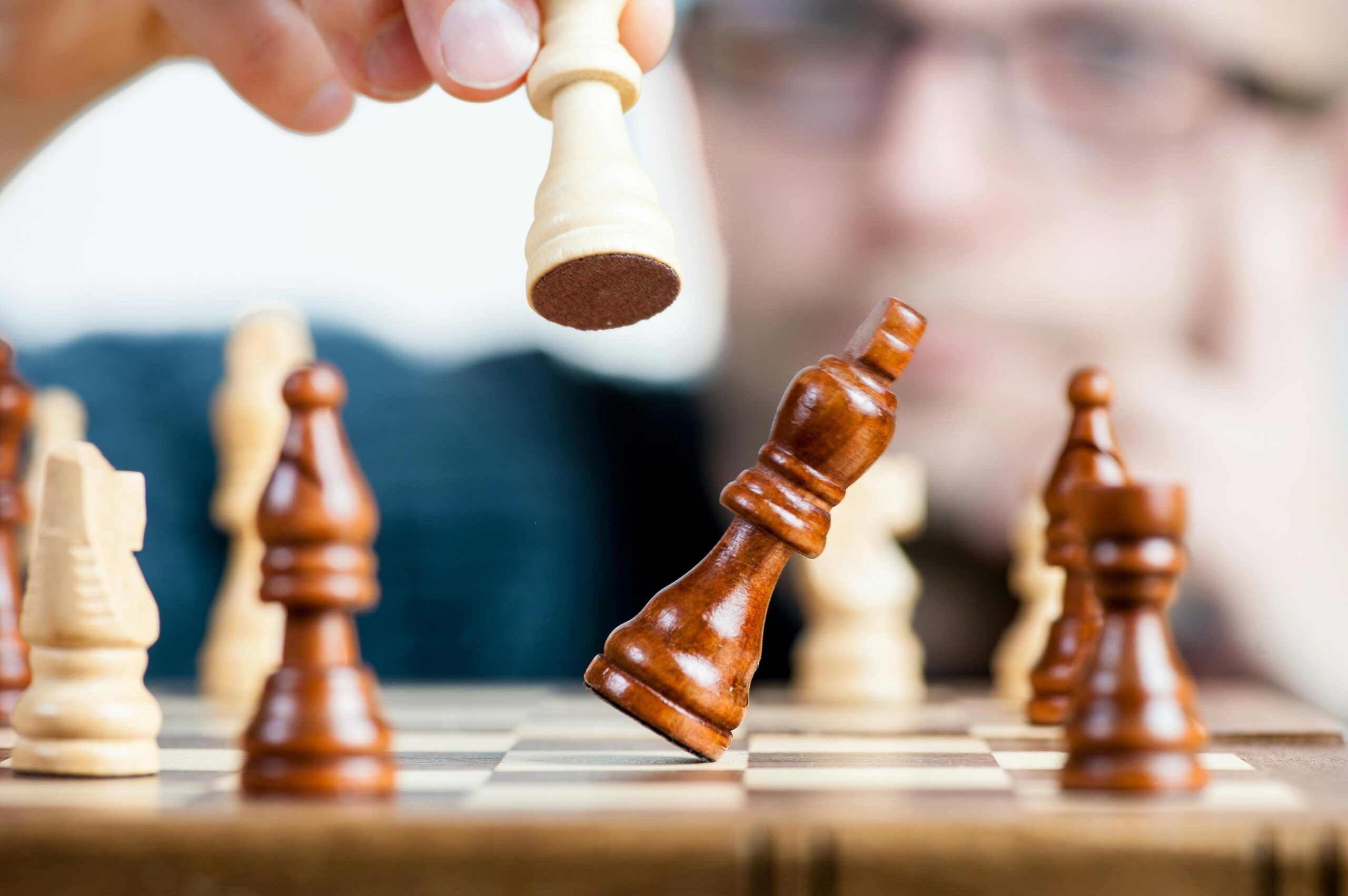 image of someone using a light wooden king chess piece to knock a dark wooden king chess piece over