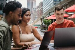 Focused young man using laptop while studying with diverse friends in outdoors cafeteria