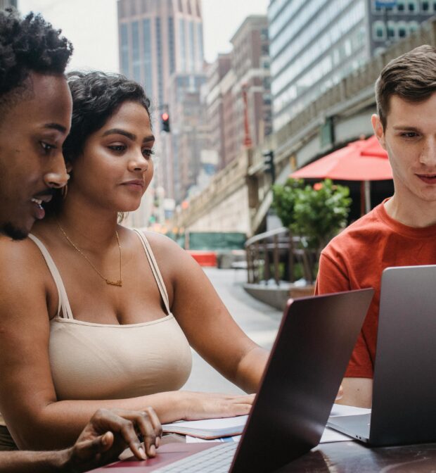 Focused young man using laptop while studying with diverse friends in outdoors cafeteria