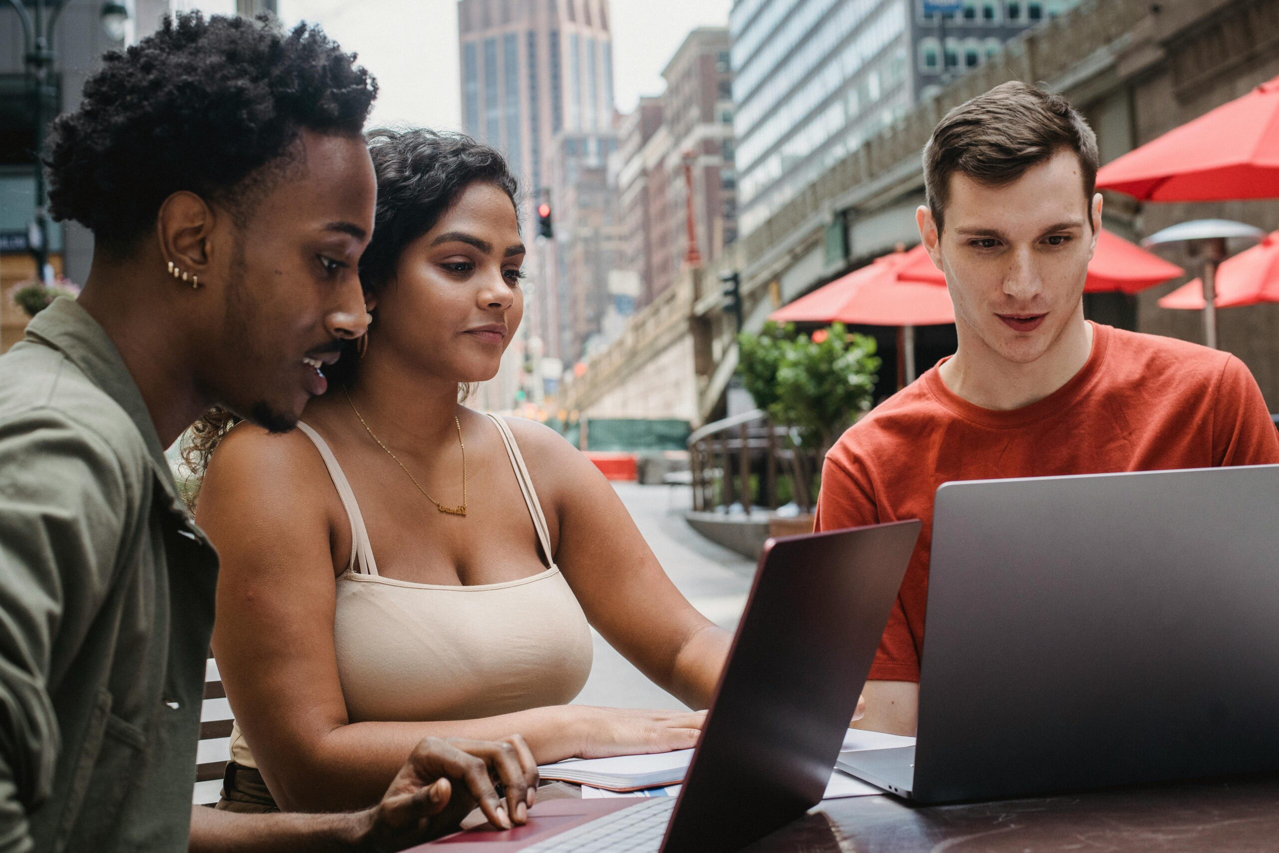 Focused young man using laptop while studying with diverse friends in outdoors cafeteria