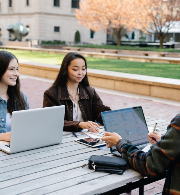 Three Young People Studying Together Outdoors With Laptops