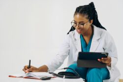 Doctor Using a Tablet and Taking Notes in a Notebook