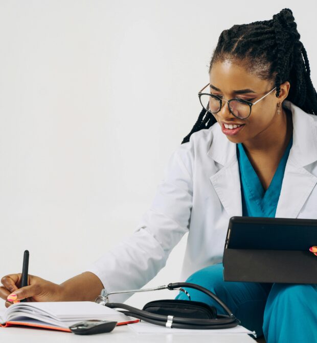 Doctor Using a Tablet and Taking Notes in a Notebook