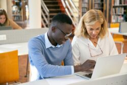 Female teacher helping male student working on laptop in library