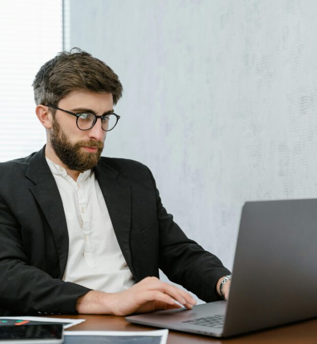 Man in Black Suit using Gray Laptop on Brown Wooden Table