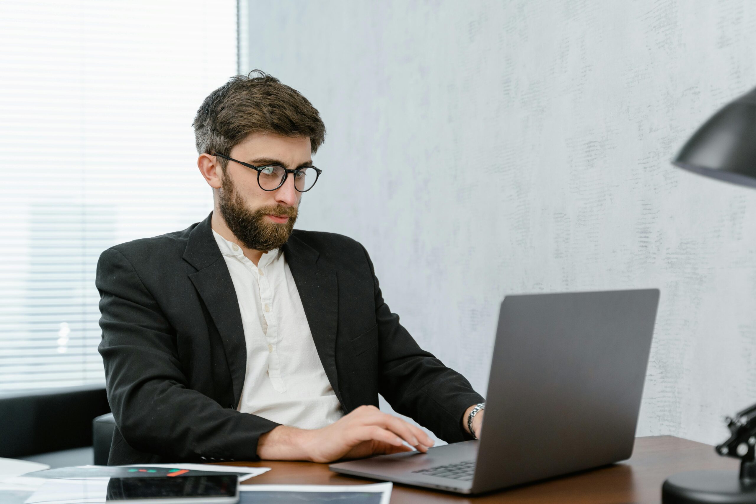Man in Black Suit using Gray Laptop on Brown Wooden Table