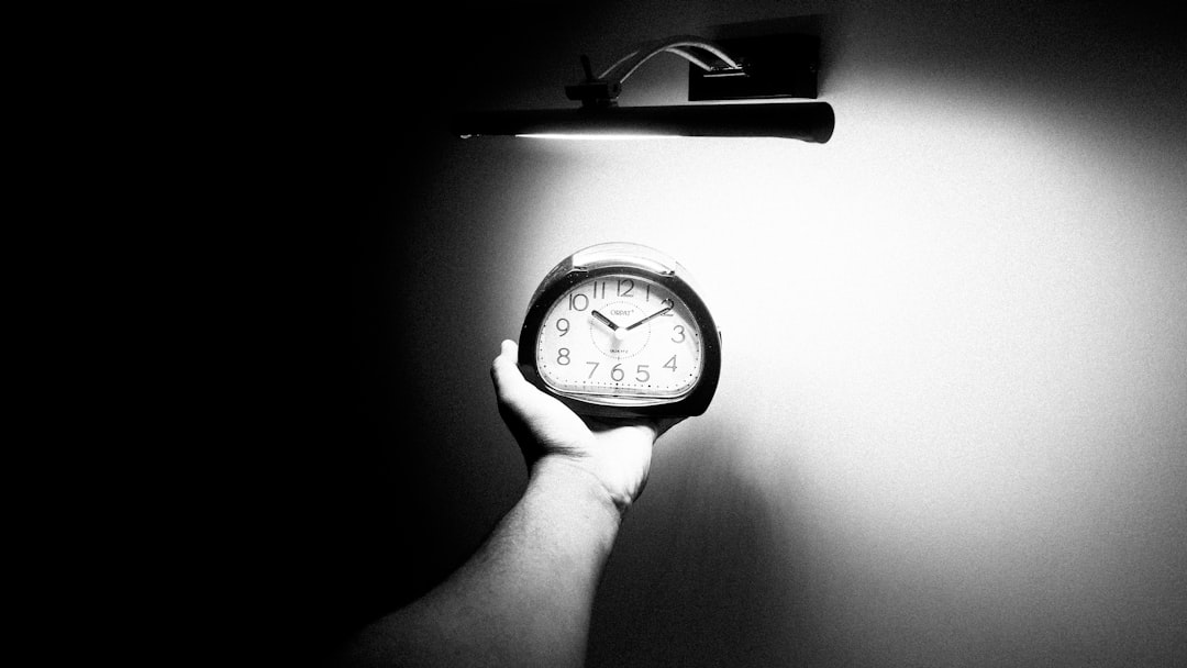 A person holding a clock in a dark setting, emphasizing the time amidst the surrounding darkness.